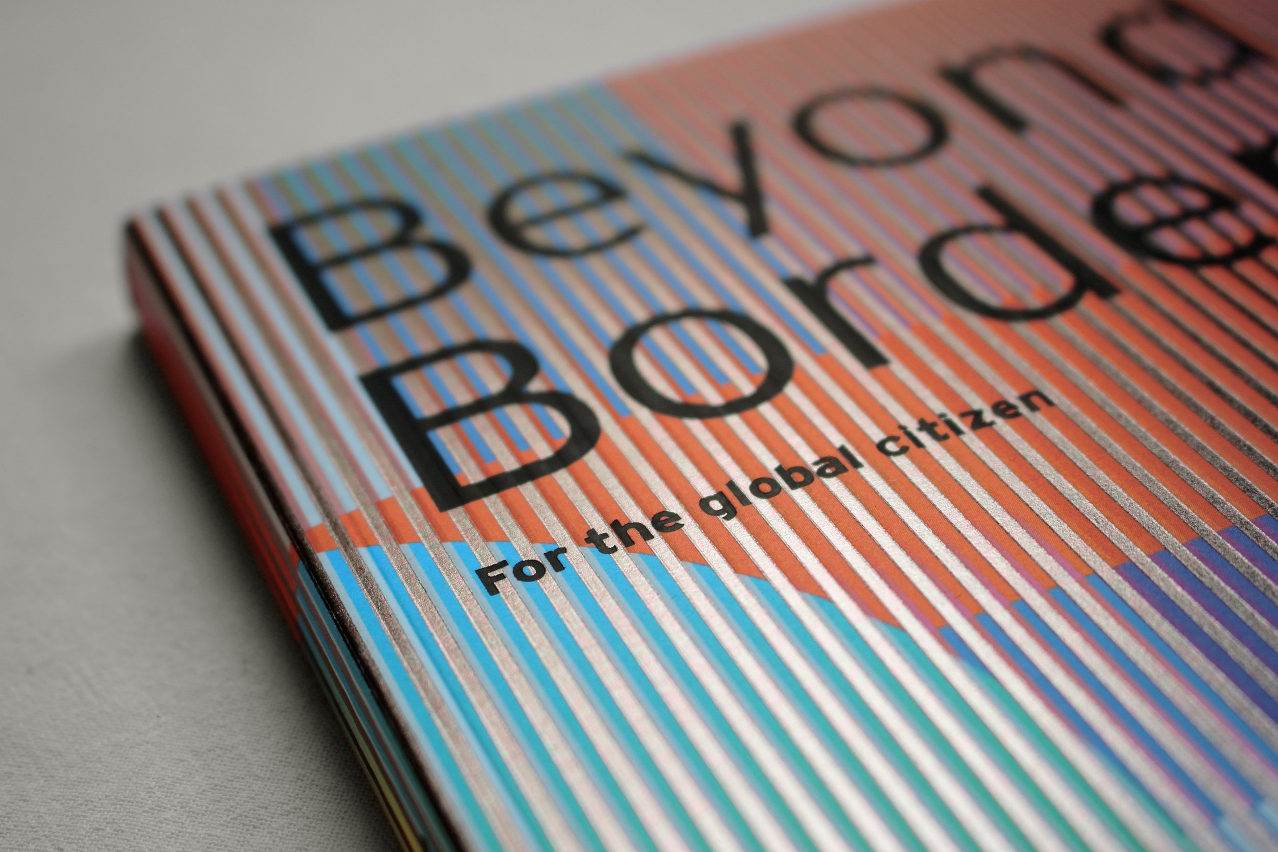 Beyond Borders cover detail: silver-foil stripes in cyan, red and blue intersecting with black sans-serif type